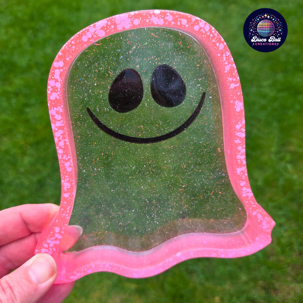 Hand holding a transparent ghost-shaped trinket tray with pink frame against a grass background