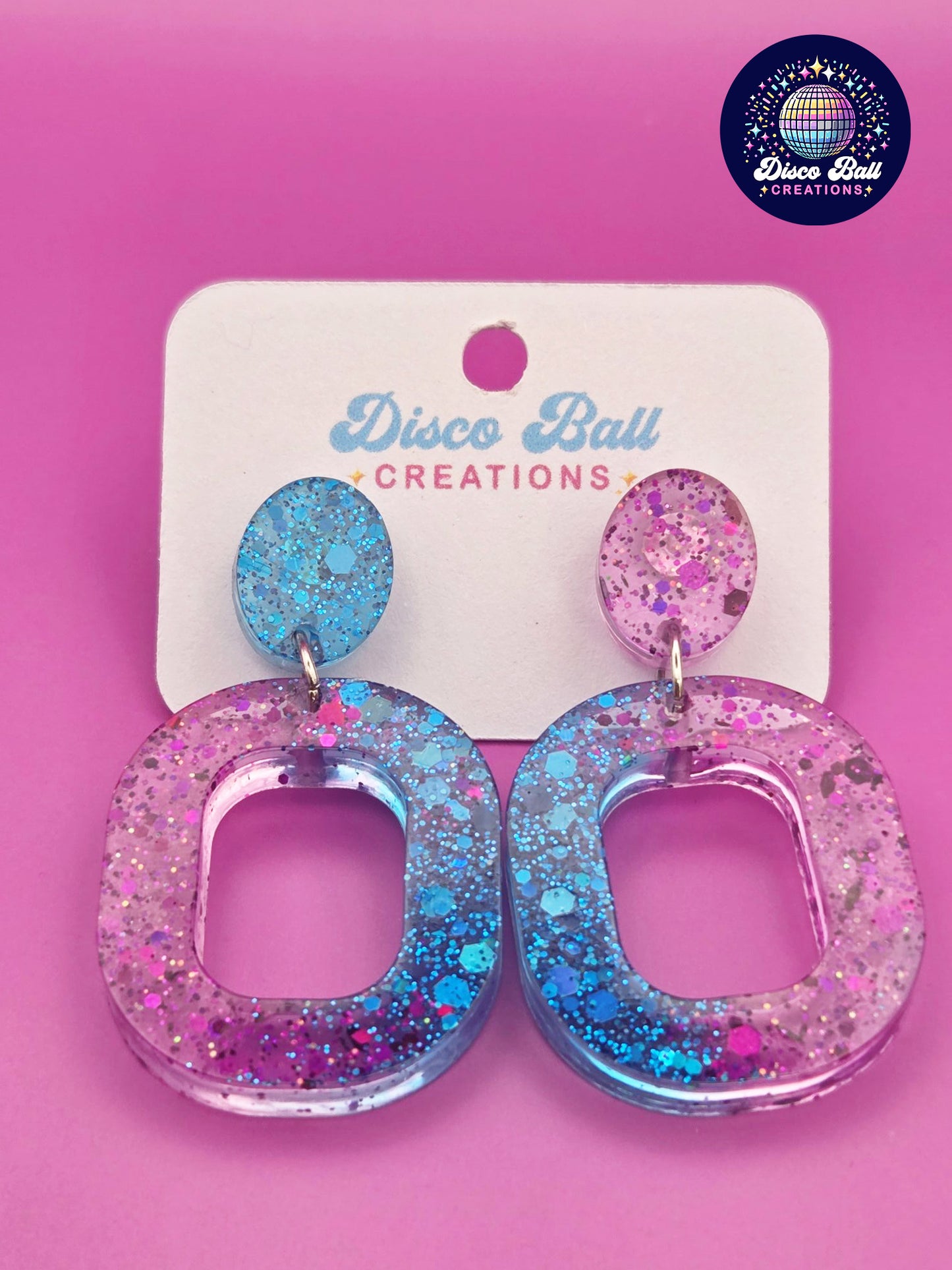 Pink and teal glitter resin oval hoop earrings with chunky sparkle, displayed on a Disco Ball Creations backing card