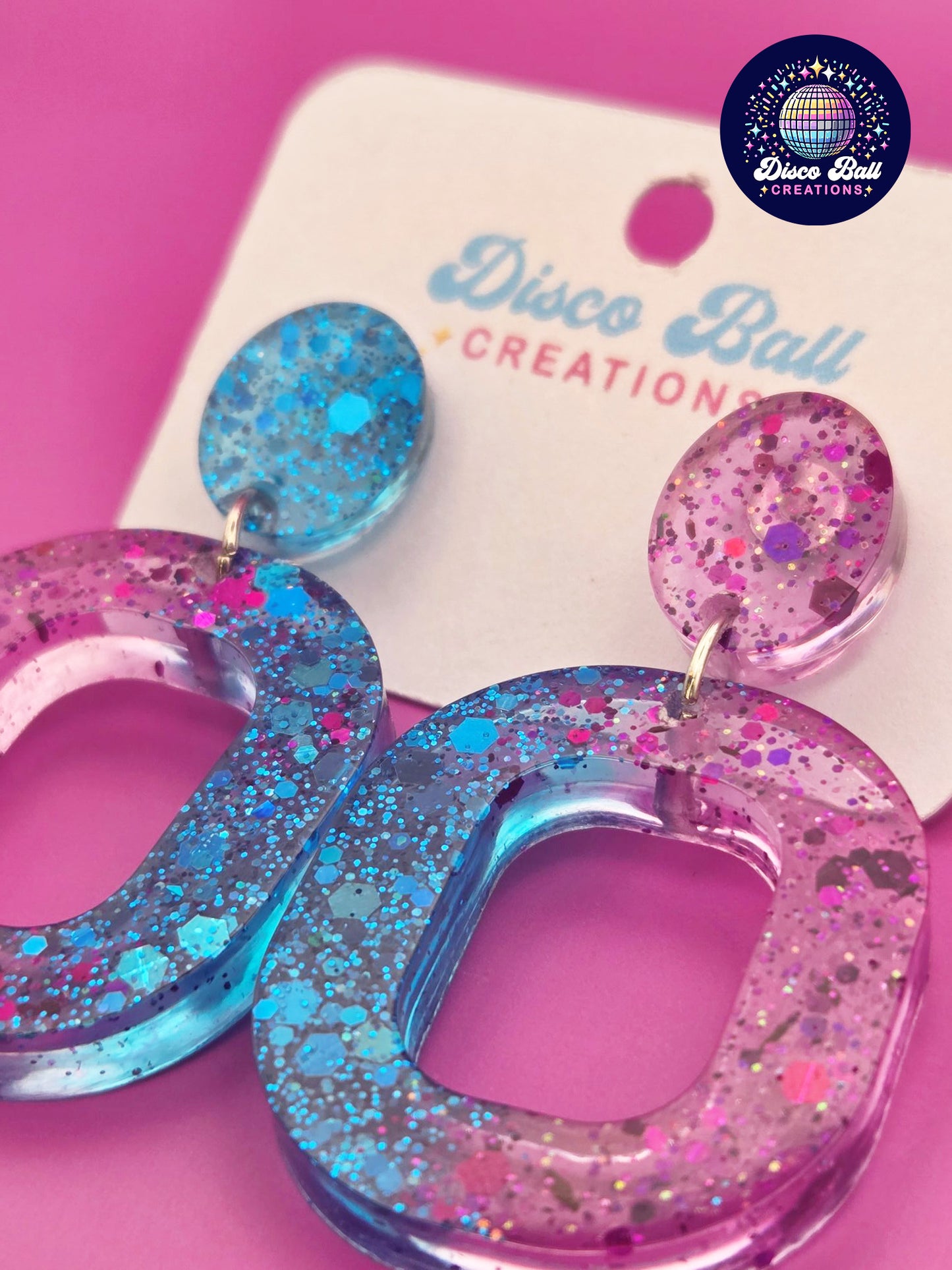 Pink and teal glitter resin oval hoop earrings with chunky sparkle, displayed on a Disco Ball Creations backing card