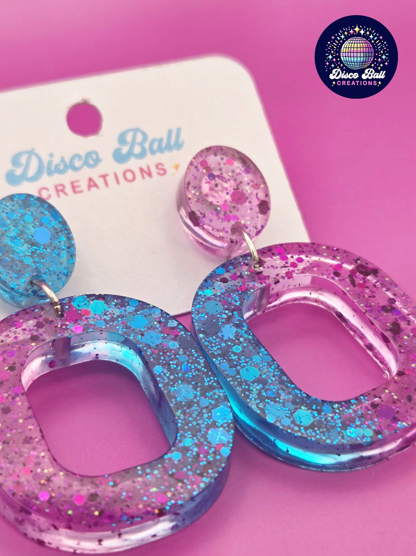Pink and teal glitter resin oval hoop earrings with chunky sparkle, displayed on a Disco Ball Creations backing card
