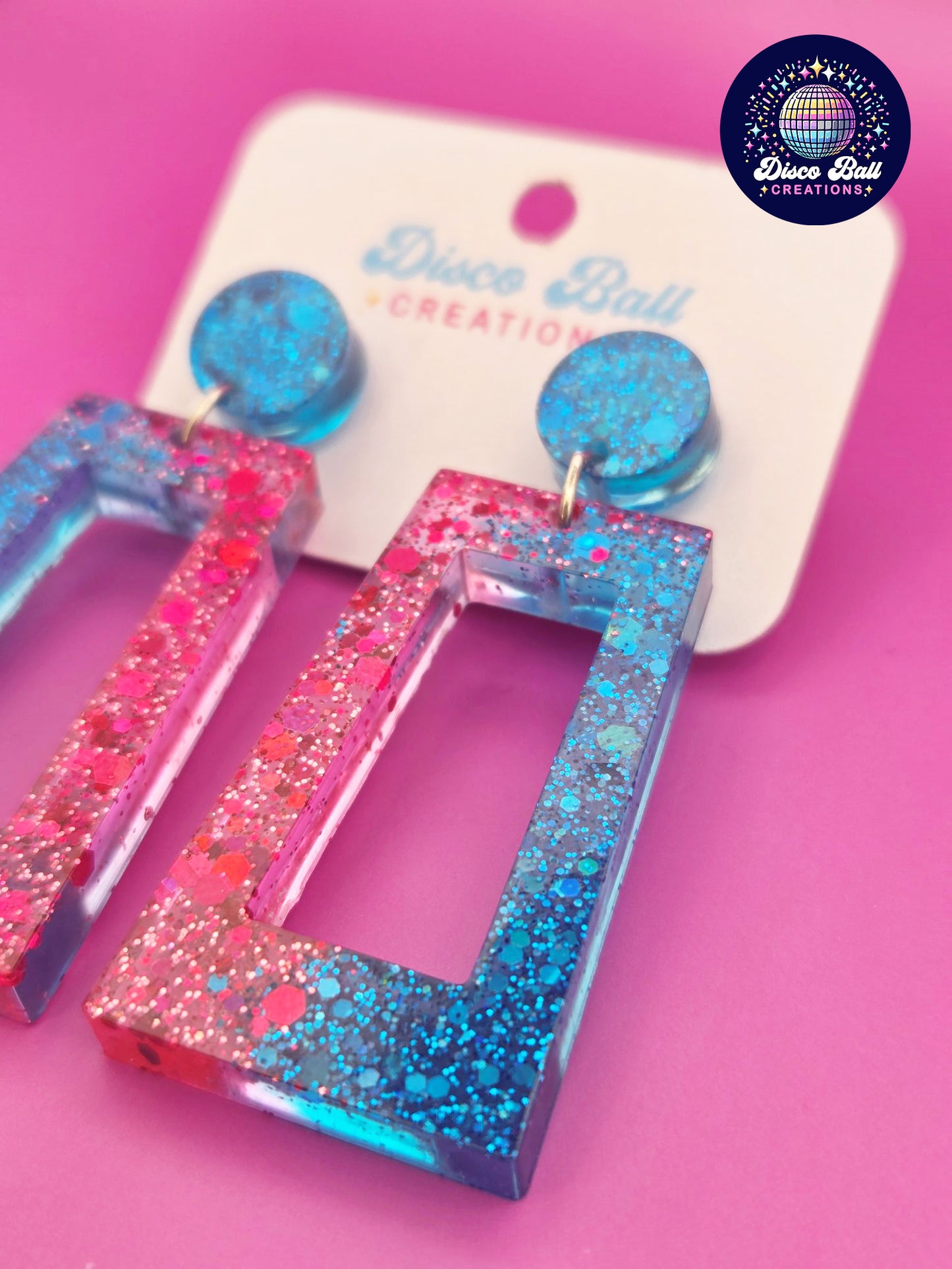 Pink and blue glitter resin rectangle earrings with geometric cut-out design, displayed on a Disco Ball Creations branded card