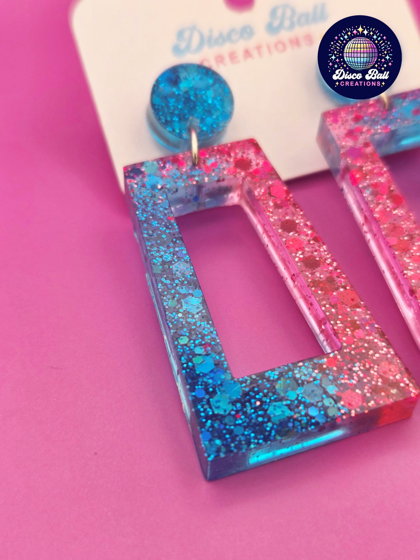 Pink and blue glitter resin rectangle earrings with geometric cut-out design, displayed on a Disco Ball Creations branded card