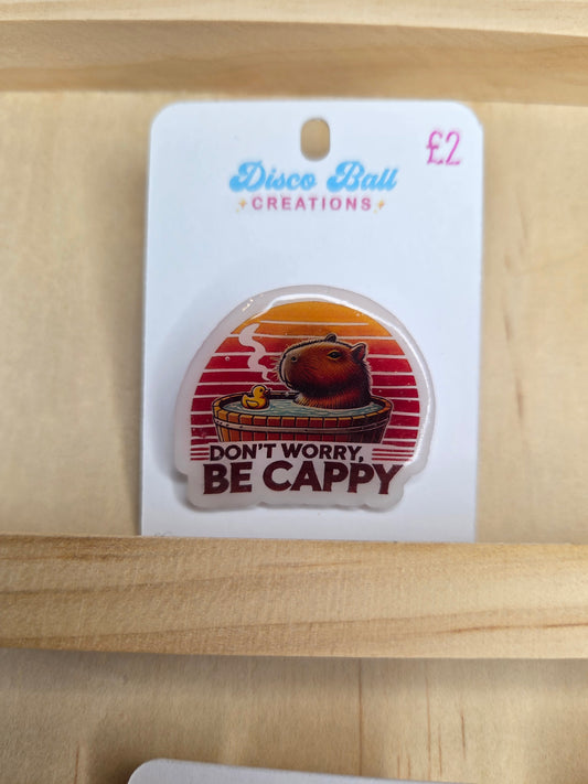 Cute capybara pin badge with the phrase “Don’t worry, be cappy” and sunset background.