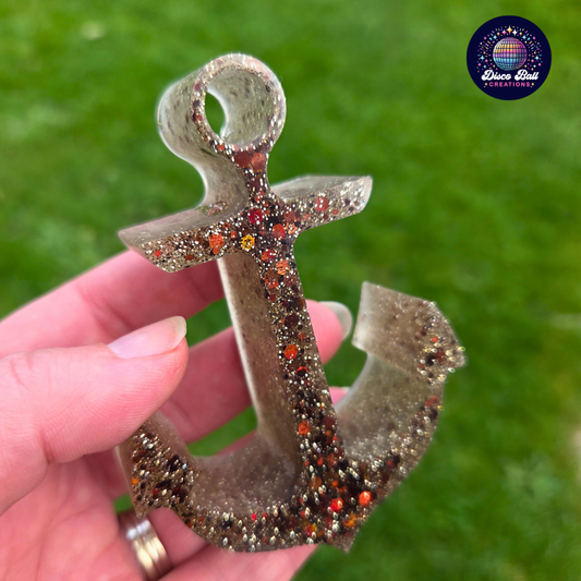 Decorative anchor with glittery embellishments held by a hand against a green background