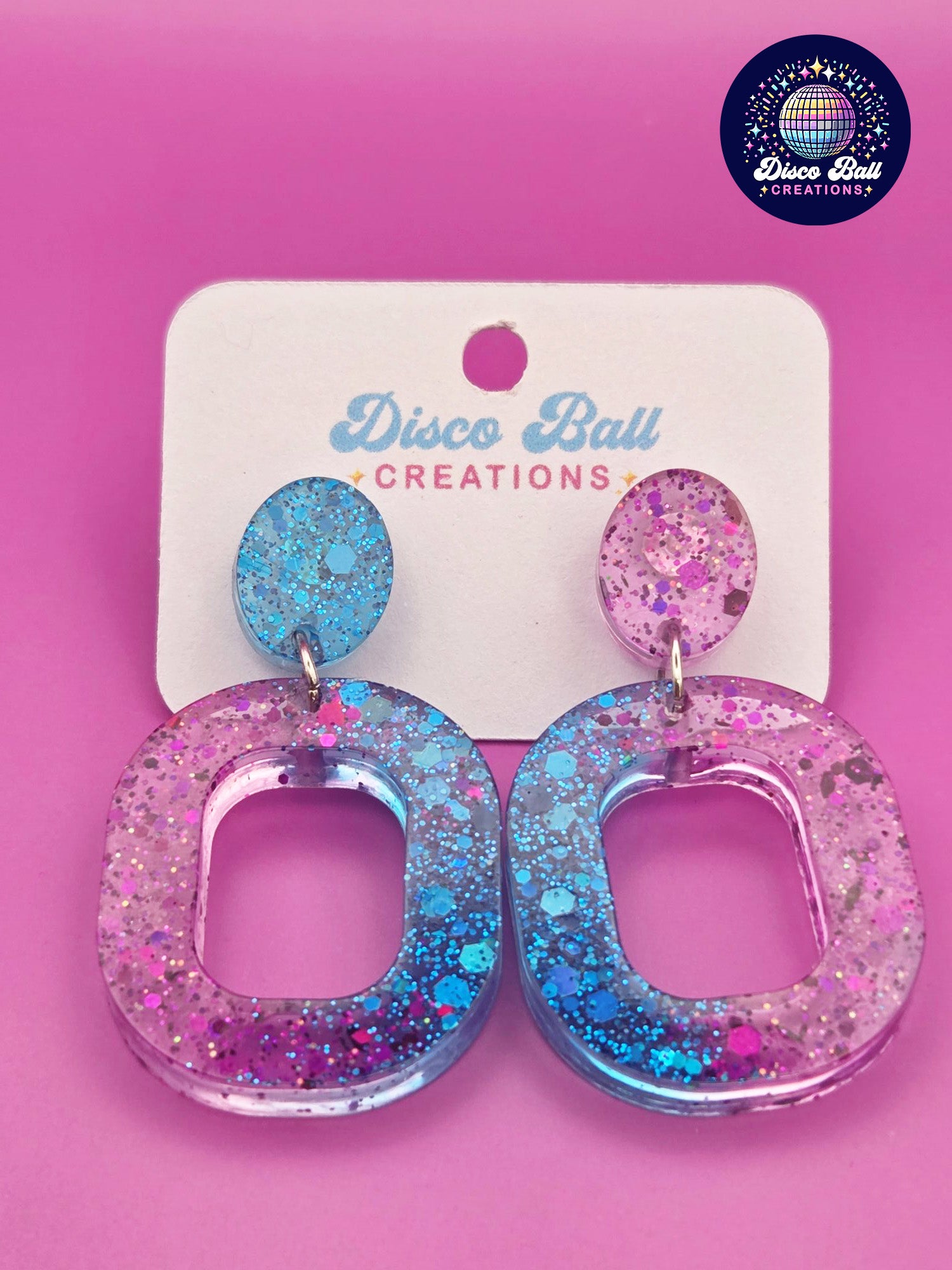 Pink and teal glitter resin oval hoop earrings with chunky sparkle, displayed on a Disco Ball Creations backing card